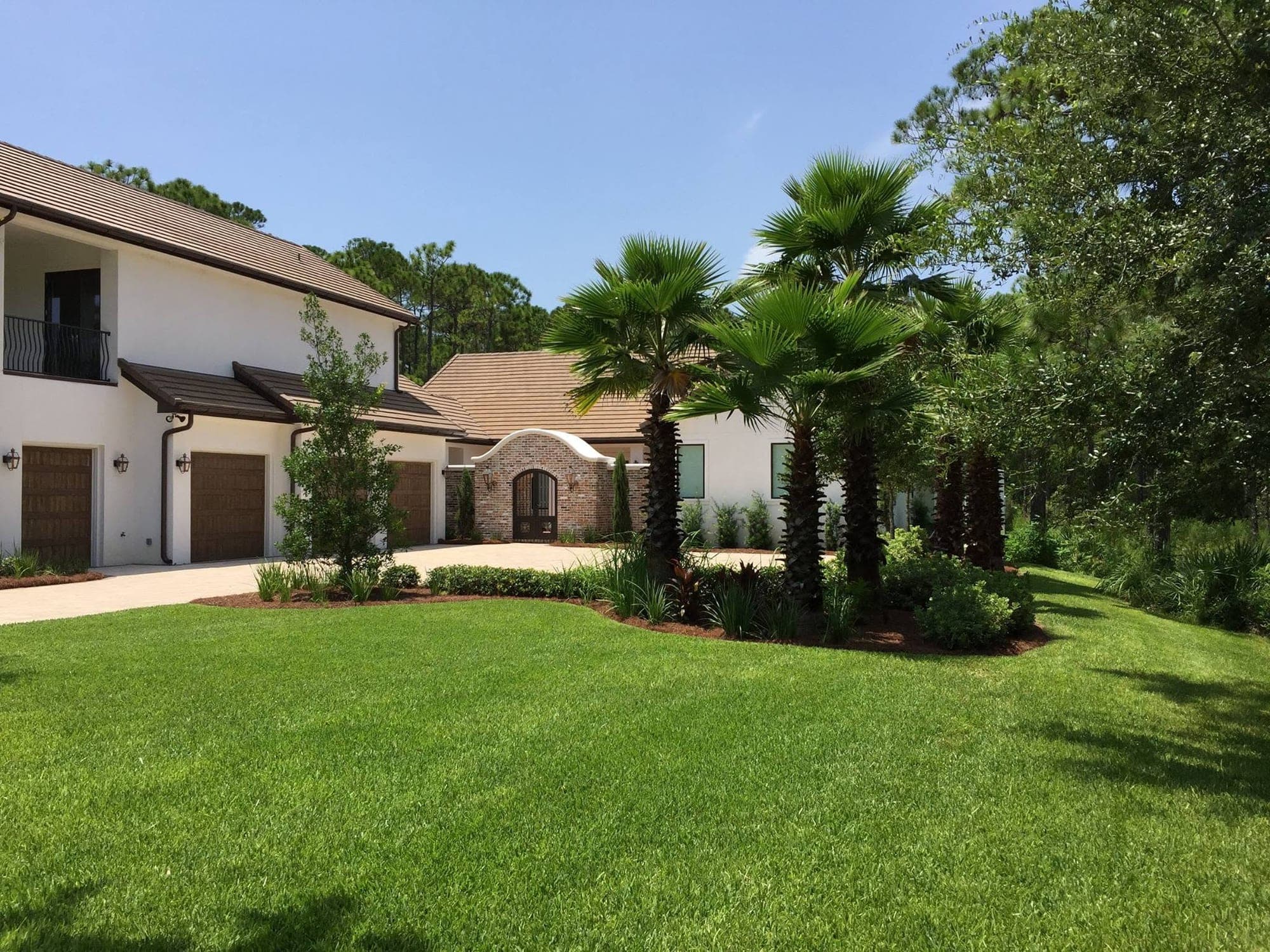 Freeport home with a brick paver driveway, fresh sod, and a grouping of palms planted along the garage side