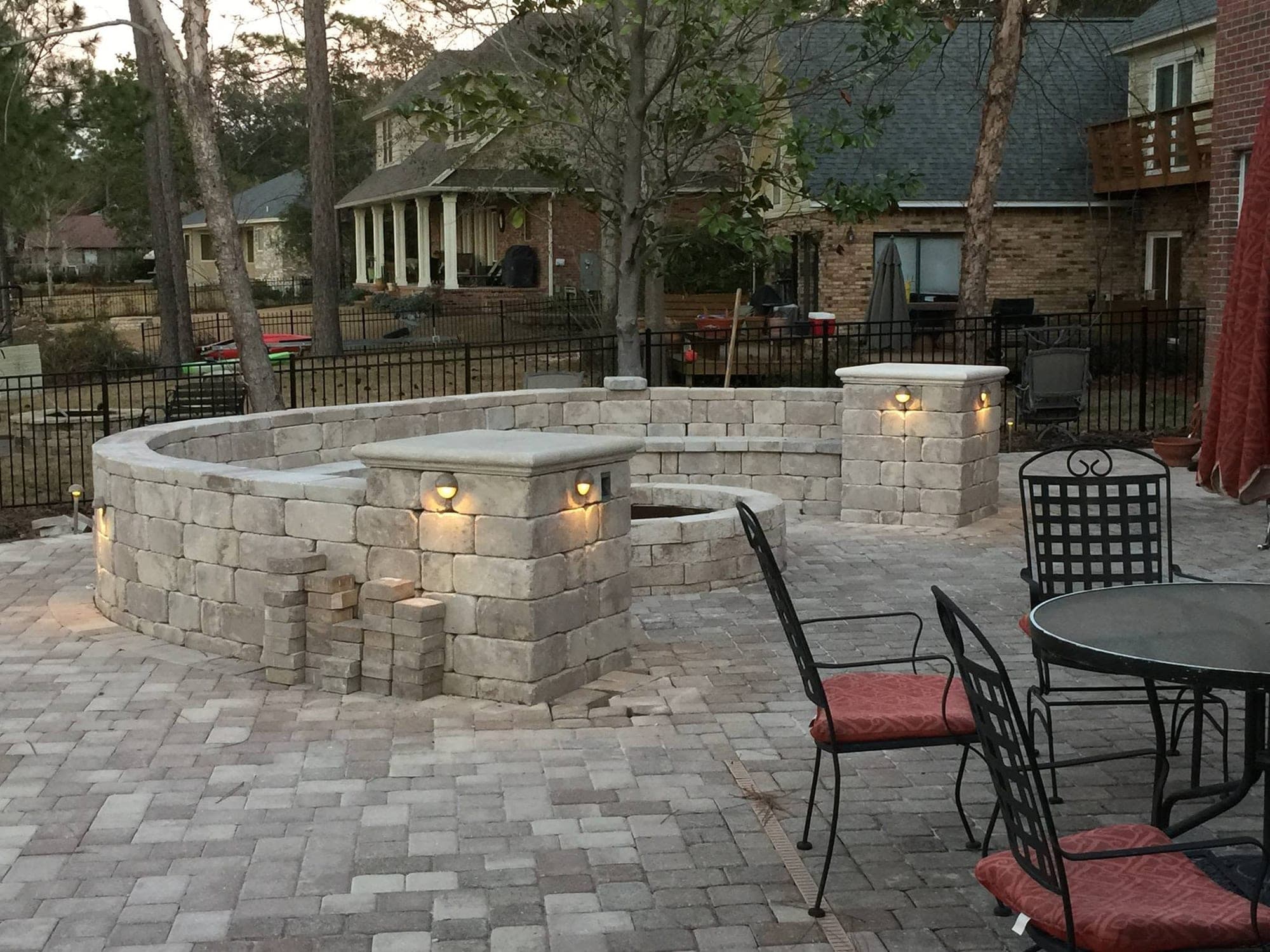Stone seat wall curving around a paver fire pit, with pillar lighting at each corner