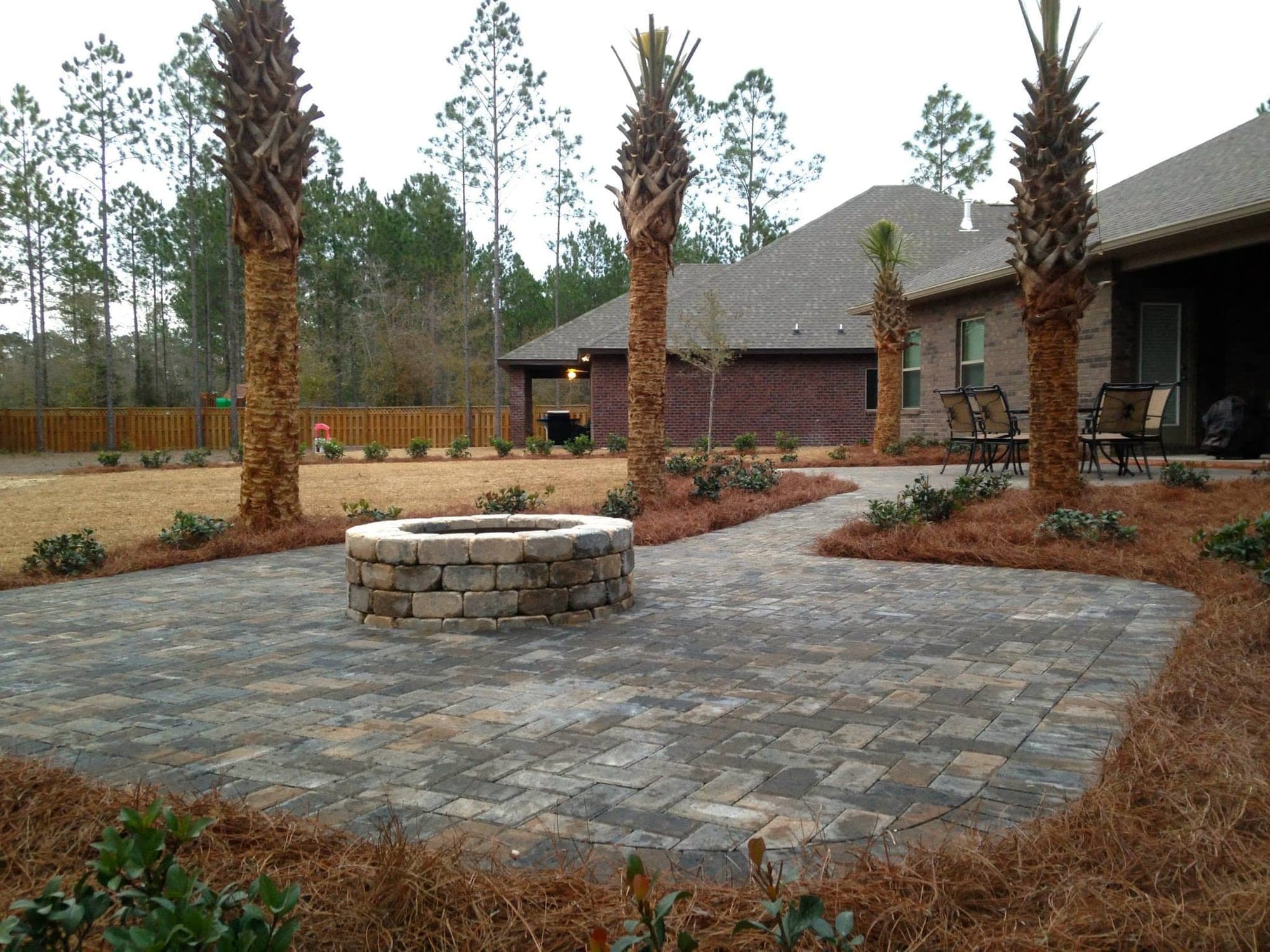 Tumbled paver patio with a built-in fire pit, surrounded by palms at a Santa Rosa Beach home